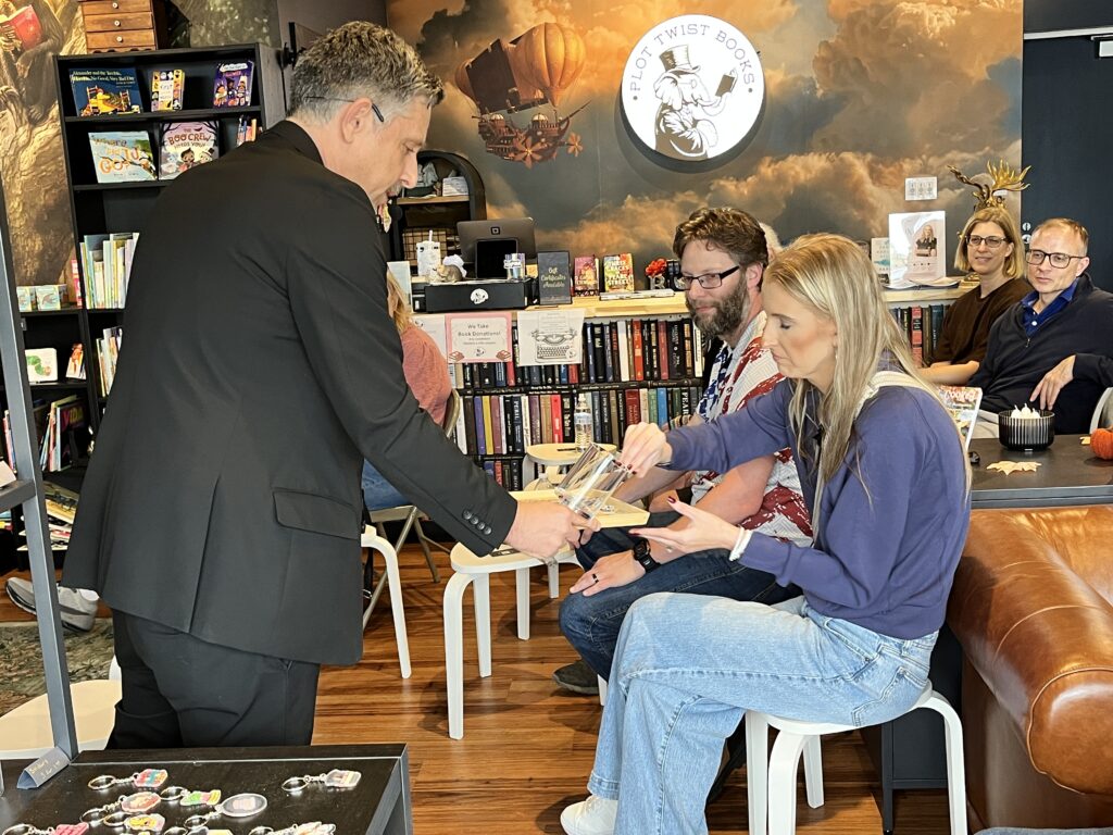 Nick Gasparro offers a clear acrylic prop to a seated volunteer as the bookstore audience watches