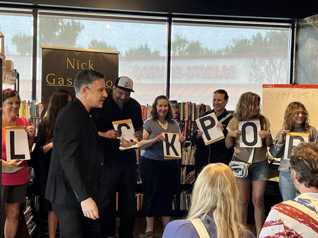 Nick Gasparro with a row of audience volunteers holding oversized letter cards during a mentalism routine