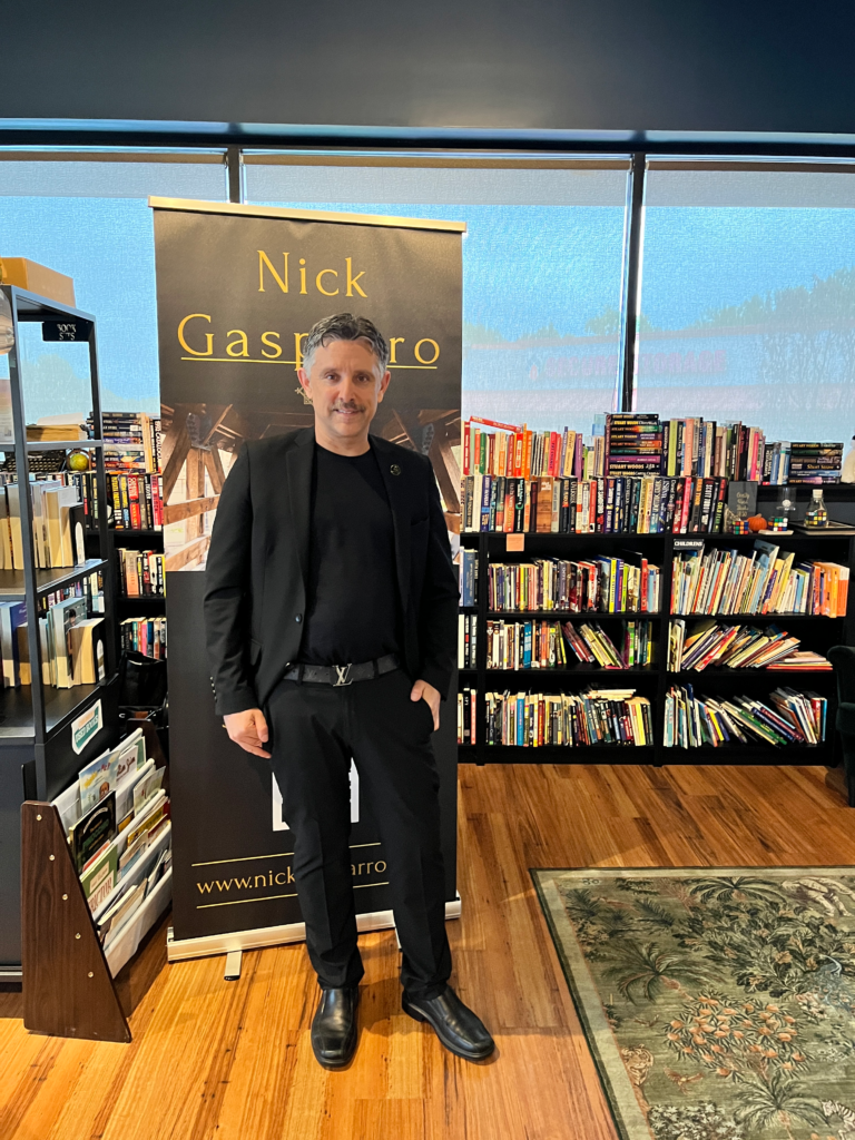 Full-length portrait of Chicago-area mentalist Nick Gasparro in front of his banner at a bookstore show