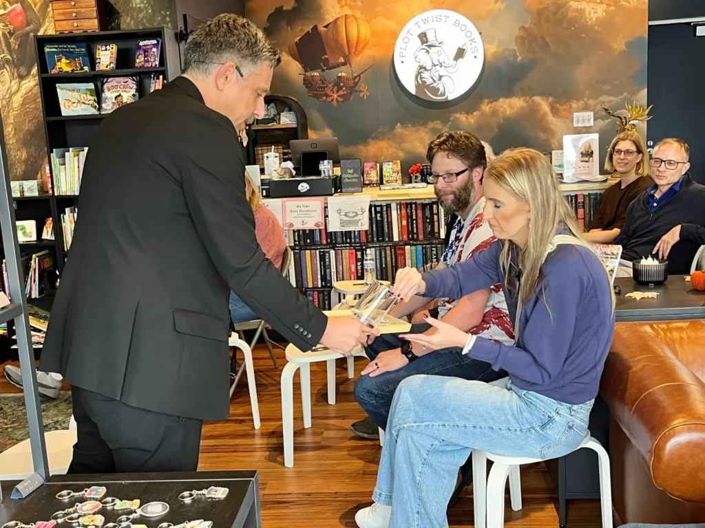 Nick Gasparro offers a clear acrylic prop to a seated volunteer as the bookstore audience watches